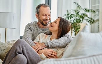 A couple embracing on the couch in the living room, smiling at each other.